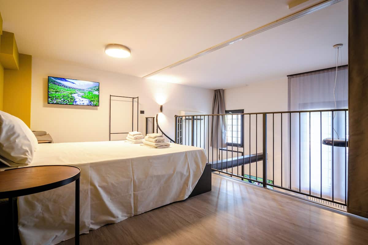 A hotel room with a bed, a TV, a balcony with a railing, and a painting on the wall.