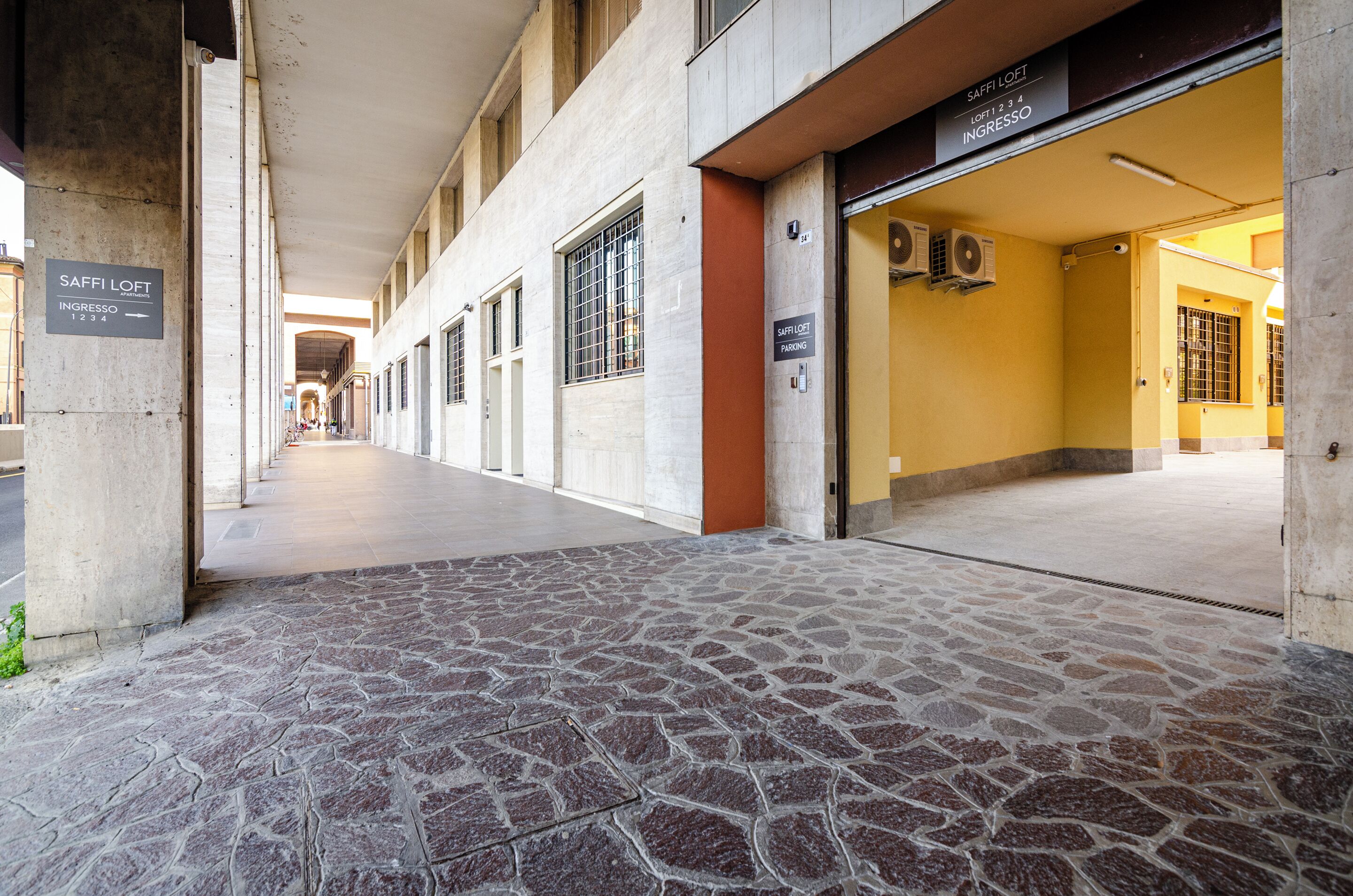 A building entrance with a stone-tiled floor, a sign for 'SAFFI LOFT INGRESSO 1234', and a parking sign.