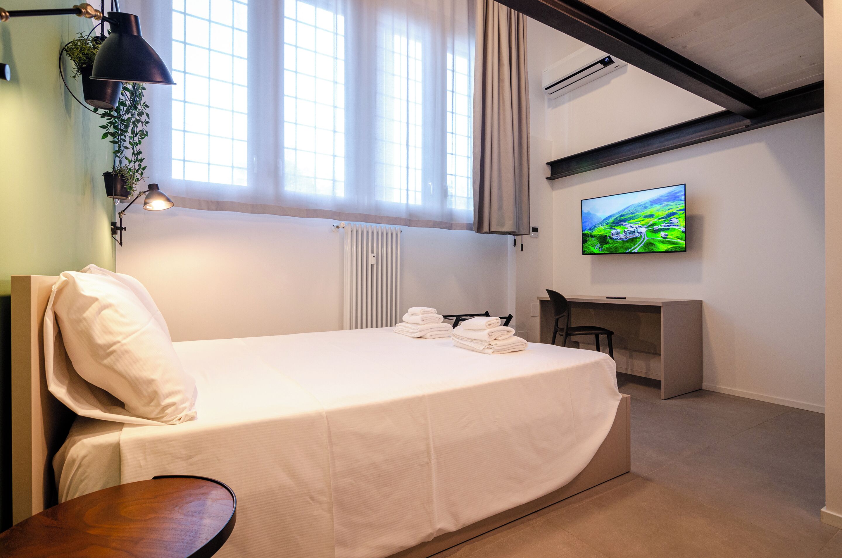 A bedroom with a bed, a desk, a TV, and a window with curtains.