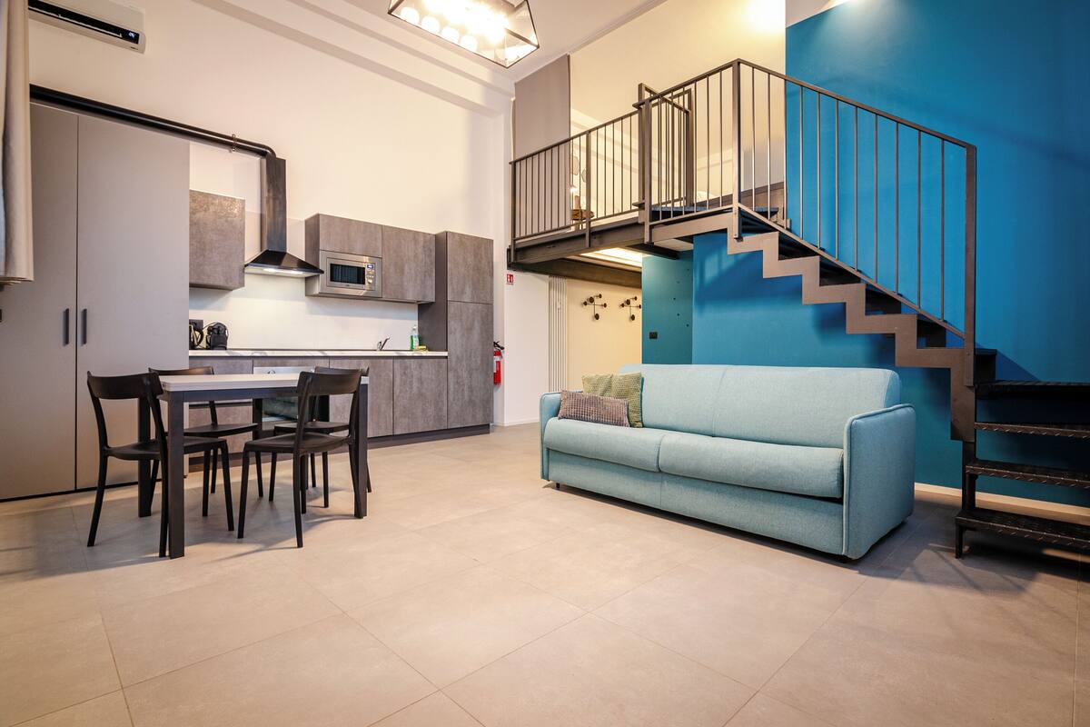 A modern kitchen with a dining area, a blue sofa, and a staircase.
