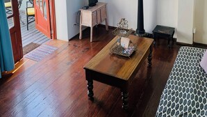 A room with a wooden floor, a small wooden table, a black TV stand, a vase with flowers, and a wall-mounted picture. - On UNESCO property 3-bedroom quaint house surrounded by gardens in Barranco (Barranco)
