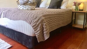 A neatly made bed with a knitted blanket, a basket of folded towels, and a bedside lamp. - On UNESCO property 3-bedroom quaint house surrounded by gardens in Barranco (Barranco)