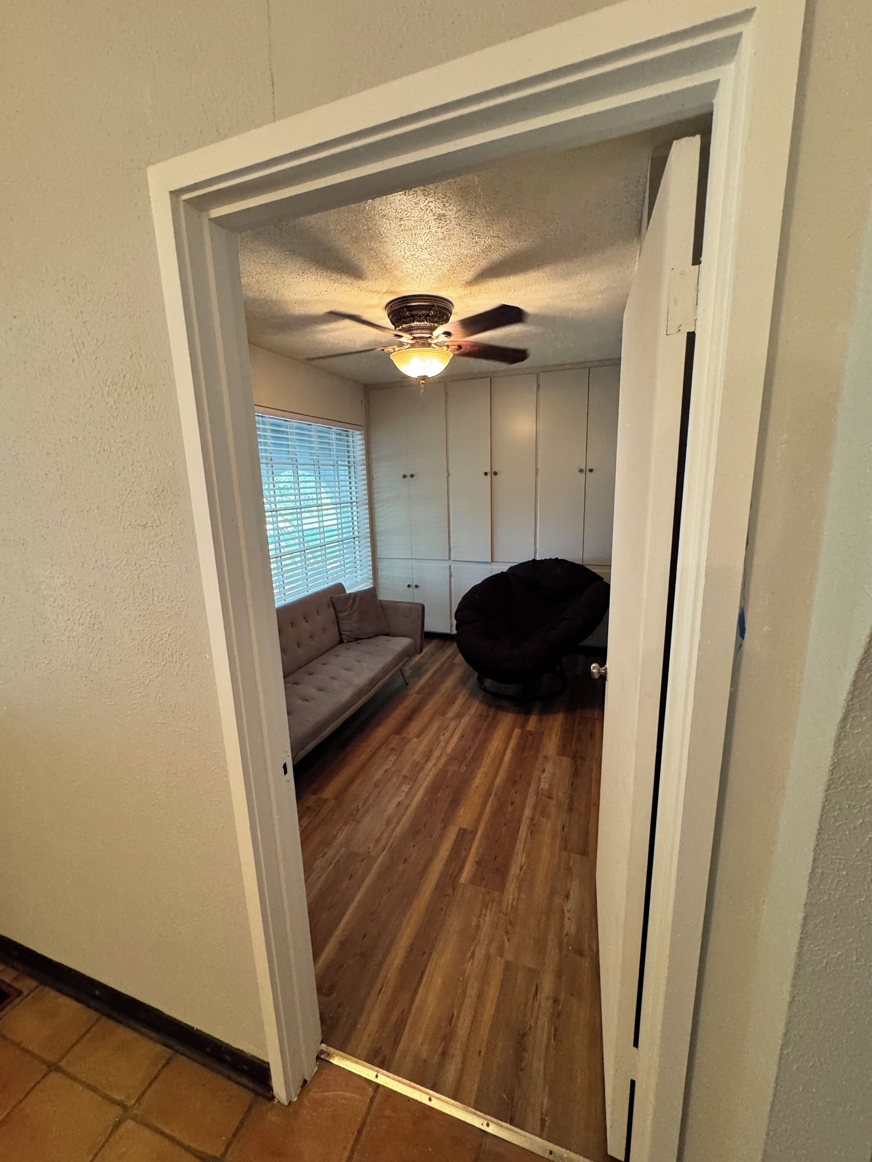 A room with a ceiling fan, a sofa, a bean bag chair, and a window with blinds.