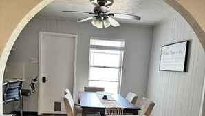 A dining area with a table, chairs, a ceiling fan, a window, and a framed quote on the wall.