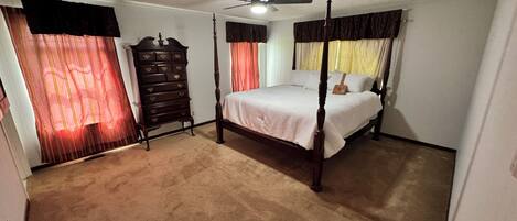 A bedroom with a four-poster bed, a dresser, and a ceiling fan.