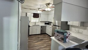 A compact kitchen with white cabinets, a microwave, a refrigerator, a ceiling fan, and a bar stool.