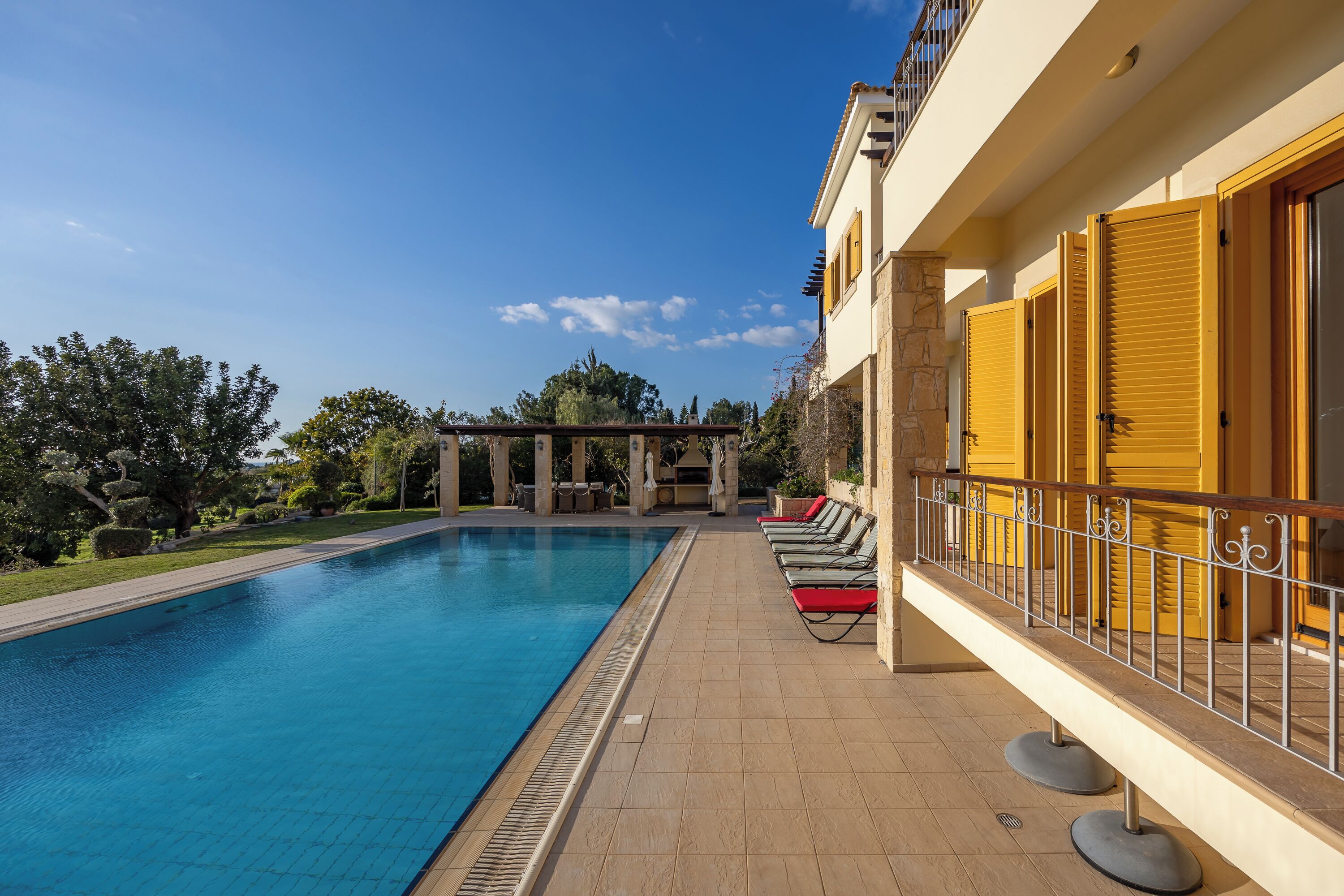 A swimming pool with a tiled deck, sun loungers, and a covered outdoor area.