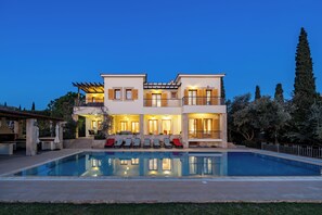 Ein zweistöckiges Haus mit Swimmingpool, Sitzgelegenheiten im Freien und einem gut beleuchteten Balkon.