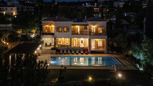 A multi-story house with a swimming pool, outdoor seating, and illuminated windows. - Villa 151 Luxury Villa - Private Pool and Tennis Court (Kouklia)