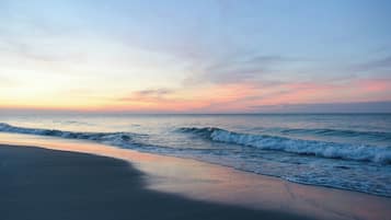 A beach with waves, a clear sky, and a sunset.
