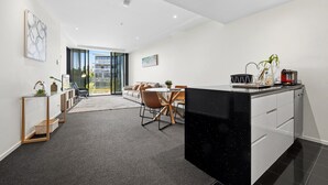 Et moderne køkken med en sort bordplade, et spiseområde med et rundt bord og stole, samt udsigt gennem en glasdør til en udendørs balkon.