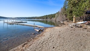 A lakeside beach with a dock, picnic tables, and a gazebo.