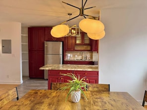 Eine Küche mit roten Schränken, einem Edelstahl-Kühlschrank, einer Granitarbeitsplatte und einem Holzespeisesaal mit einem Blumentopf.