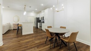 A modern kitchen with white cabinets, a central island, and a dining area with a round table and chairs. - Executive condo...traveling professionals, look no further! (Valdosta)
