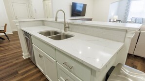 A modern kitchen with a double sink, white cabinetry, and a television mounted on the wall. - Executive condo...traveling professionals, look no further! (Valdosta)