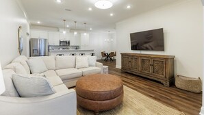 A modern living room with a sofa, ottoman, wooden cabinet, and a flat-screen TV mounted on the wall. - Executive condo...traveling professionals, look no further! (Valdosta)