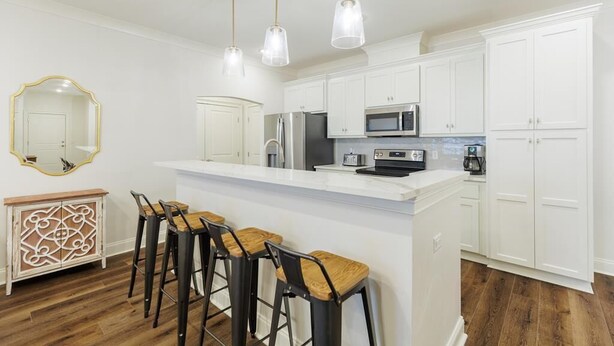 A modern kitchen with white cabinets, a central island with stools, and pendant lighting. - Executive condo...traveling professionals, look no further! (Valdosta)