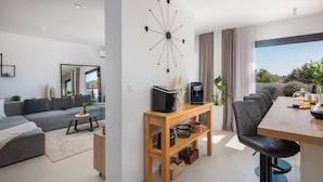 Uma sala de estar moderna com sofá, mesa de centro e uma área de jantar com um banquinho.