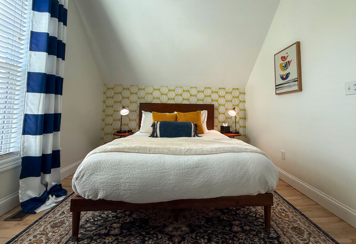 Ein Schlafzimmer mit Bett, Nachttischlampen, einer Wand mit Muster, einem Vorhang und einem gerahmten Bild.