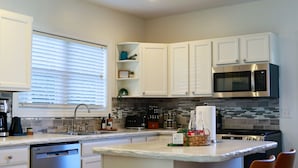 A modern kitchen with white cabinets, a stainless steel dishwasher, a microwave, and a central island with bar stools. - Modern, cozy, 2 bedroom, 1 bath home in Central Elkhart.  (Elkhart)