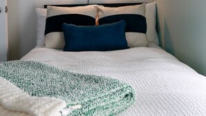 A bed with a white and green blanket, a blue pillow, and a wall-mounted light fixture. - Modern, cozy, 2 bedroom, 1 bath home in Central Elkhart.  (Elkhart)
