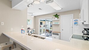 Una cucina con piano di lavoro bianco, lavello in acciaio inossidabile e frigorifero. Si vede una finestra con vista su una casa e una porta che dà su un balcone.