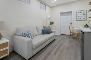 A modern living room with a sofa, a dining area with a table and chairs, and a kitchen area with a sink and countertop.