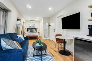 A modern hotel room with a bed, a sofa, a coffee table, a TV, and a dining area.
