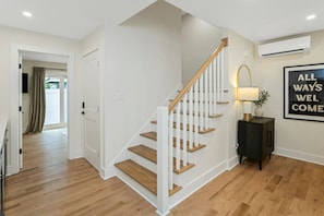 Eine Treppe mit Holzhäuschen und weißen Geländern, ein Korridor mit Holzboden, eine Tür zu einem Zimmer und eine Wand-Klimaanlage.