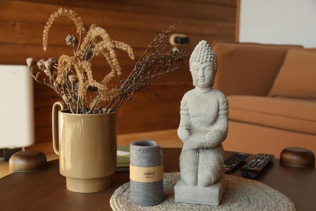 A statue of Buddha, a candle, and dried flowers on a table.