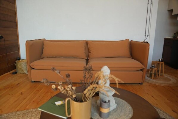 A living room with a brown sofa, a coffee table with a book and a vase, and a small wooden stool.