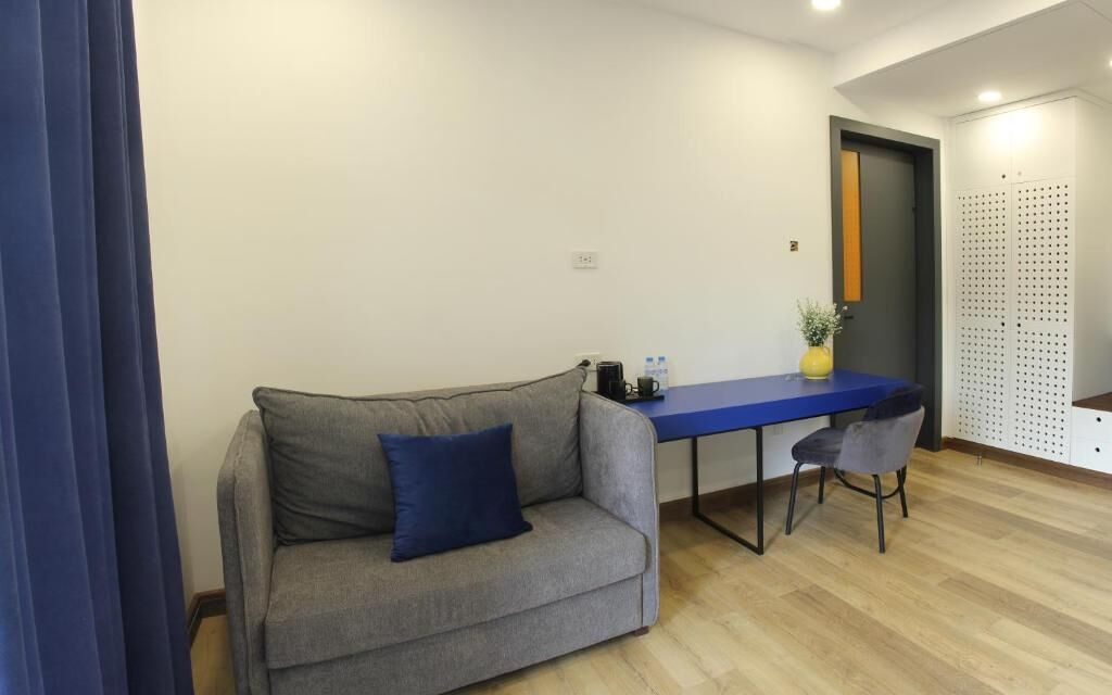 Ein Zimmer mit einem grauen Sofa, einem blauen Tisch, einem Stuhl, einer kleinen Pflanze und einer Tür mit einer Zierverkleidung.