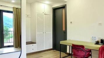 Um quarto com escrivaninha, cadeira, janela com cortinas, porta e espelho fixado na parede.