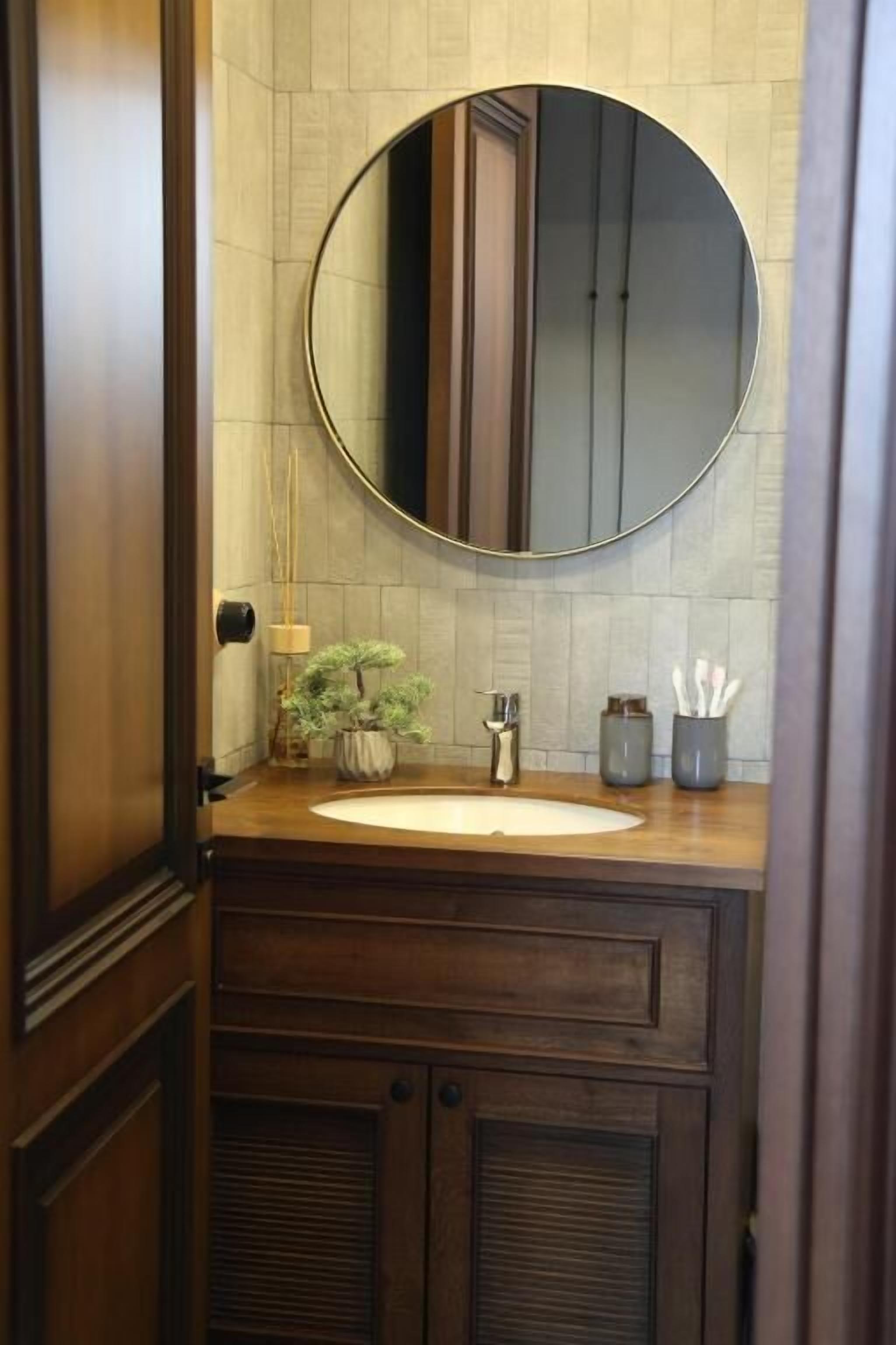 Une salle de bain avec un miroir rond, un meuble-lavabo en bois et une plante en pot.