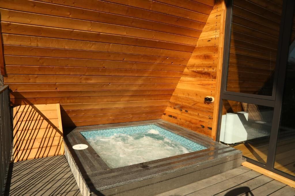 Een houten hut met een bubbelbad en een glazen deur.