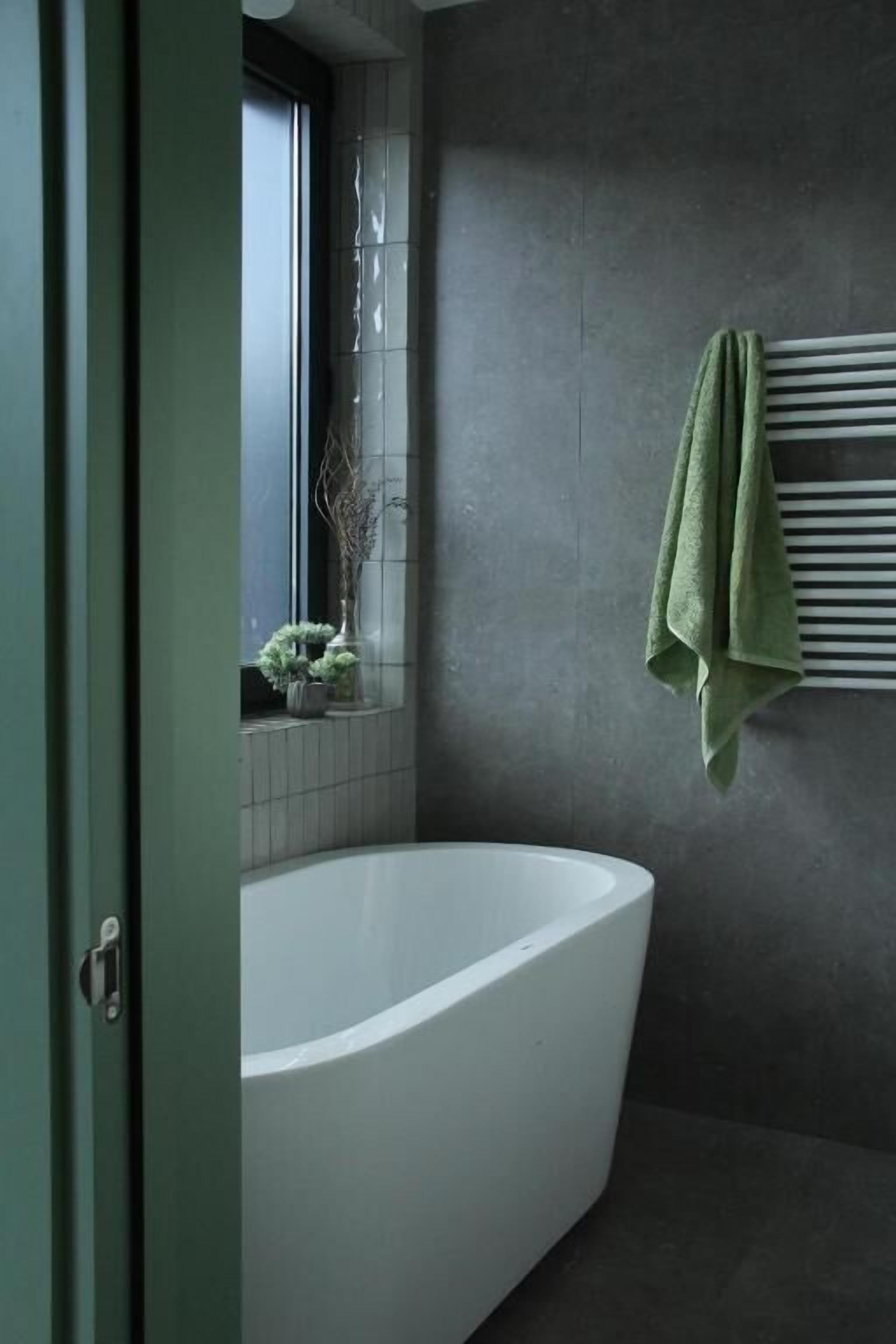 Ein modernes Badezimmer mit freistehender Badewanne, einem Fenster mit Pflanzen und einem Handtuchhalter.