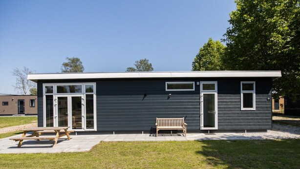 A modern building with a flat roof, large glass doors, and a bench in front. - Lessenaar 22 | 6 persoons chalet in Zennewijnen (Zennewijnen)