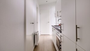 A narrow hallway leading to a kitchen with white cabinetry and a built-in oven. - Lessenaar 22 | 6 persoons chalet in Zennewijnen (Zennewijnen)