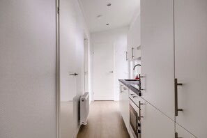 Ein schmaler Flur führt zu einer Küche mit weißen Schränken und einem eingebauten Backofen.