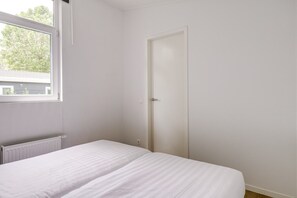 A bedroom with a bed, a window, a radiator, and a door. - Lessenaar 22 | 6 persoons chalet in Zennewijnen (Zennewijnen)