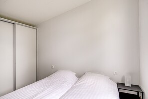 Ein schlicht eingerichtetes Schlafzimmer mit Bett, Nachttisch und Kleiderschrank.
