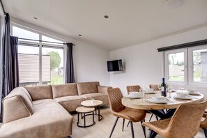Ein modernes Wohnzimmer mit einem Ecksofa, einem runden Esstisch für vier Personen und einem flachbildfernseher an der Wand.