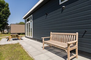 A wooden bench and picnic table outside a building with dark siding and large windows. - Lessenaar 22 | 6 persoons chalet in Zennewijnen (Zennewijnen)