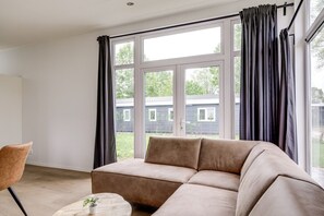 Ein modernes Wohnzimmer mit einem beigefarbenen Sofa, einem runden Couchtisch und Blick auf ein Haus durch große Fenster.