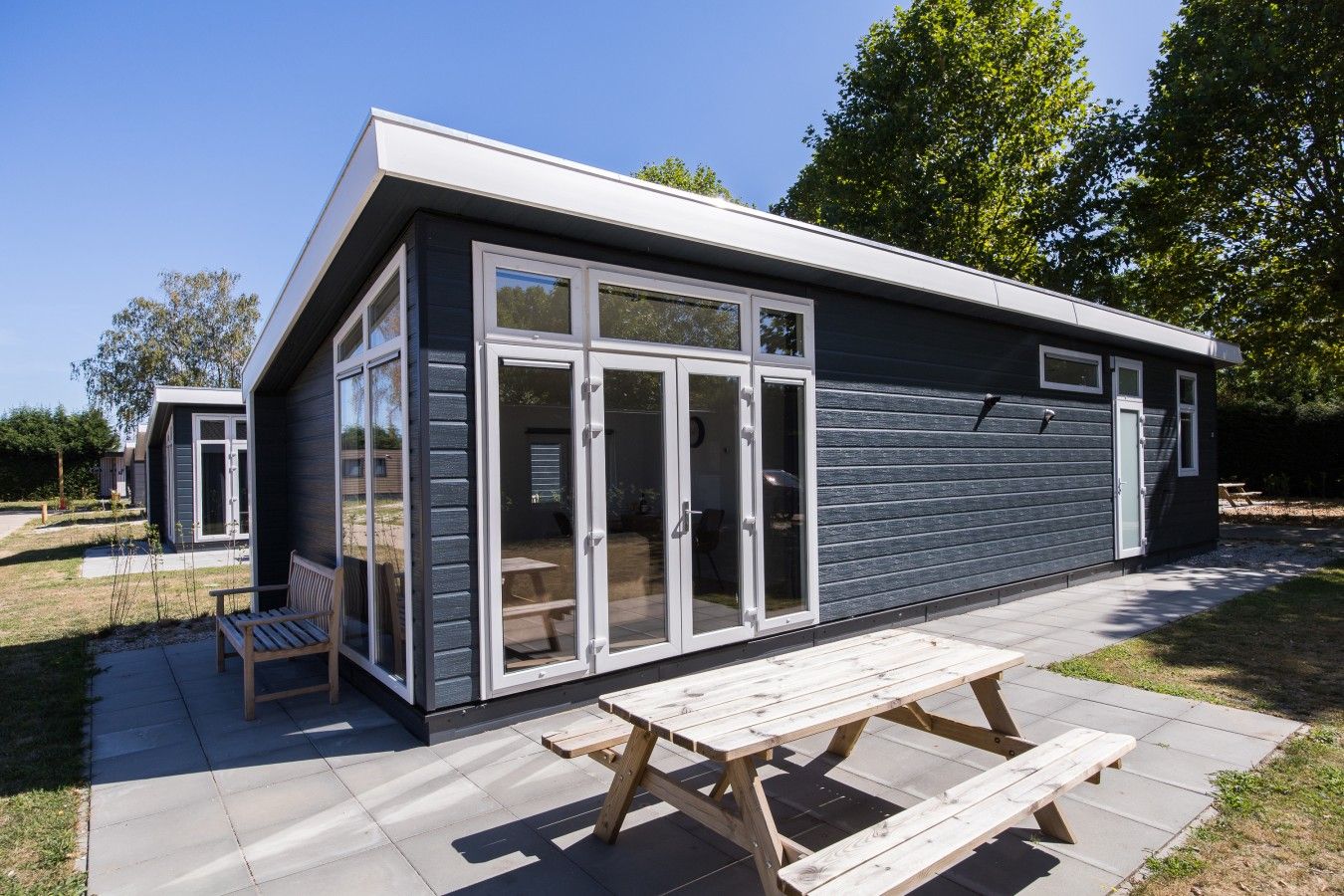 A modern building with large glass doors and a patio area with a wooden table.