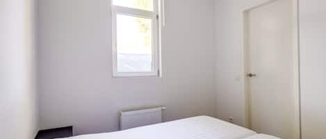 Una habitación pequeña con cama individual, ventana, radiador y puerta.