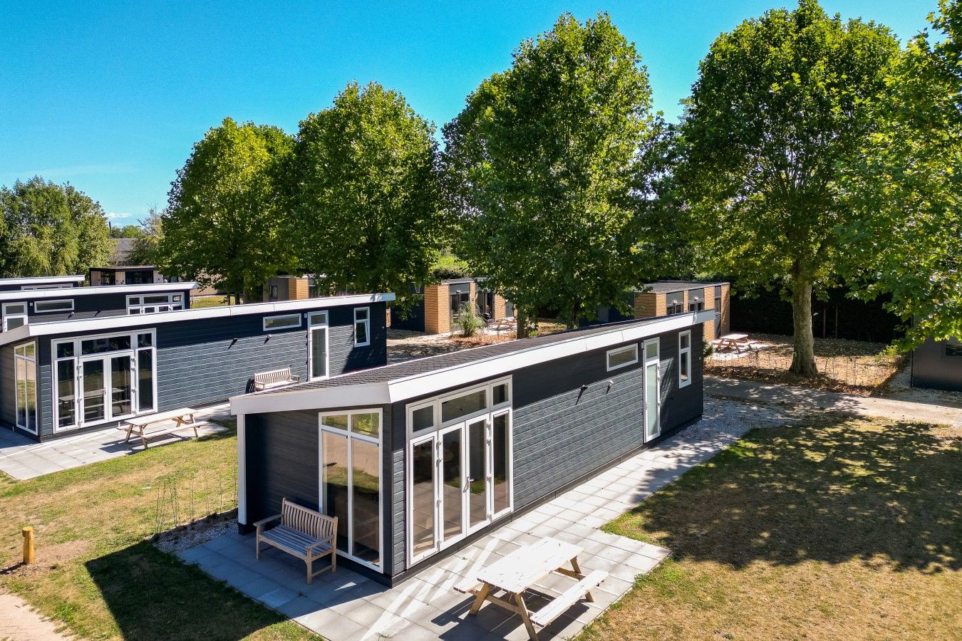 Un complexe résidentiel moderne composé de plusieurs maisons à deux étages, dotées de grandes fenêtres en verre et entourées d’une pelouse bien entretenue.