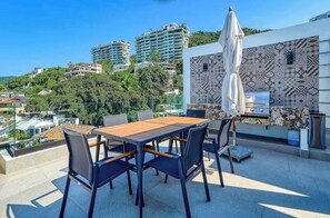 Una terrazza sul tetto con tavolo e sedie di legno, un barbecue e piastrelle decorate.