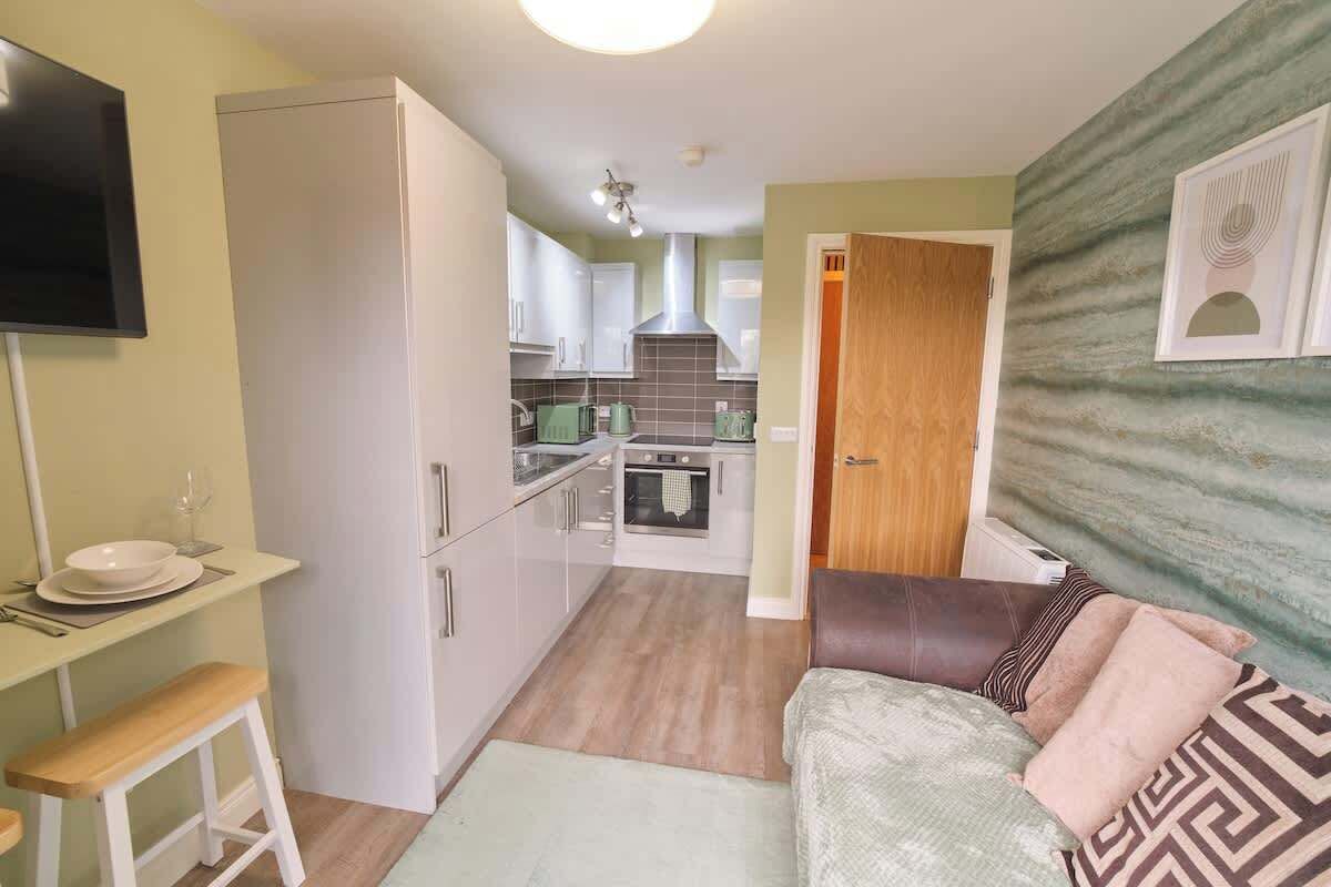 A compact living space with a kitchenette, a dining area with a table and chairs, and a sofa with cushions.