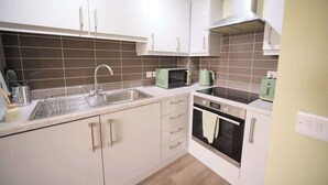 Una cucina compatta con mobili bianchi, un lavello in acciaio inossidabile, un forno a microonde e un forno.